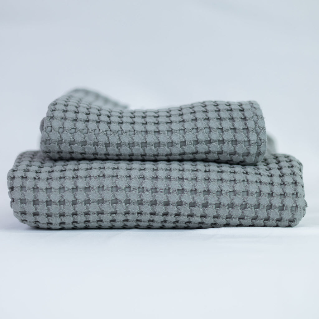 Two grey textured towels, one body and one hand, stacked against a white background