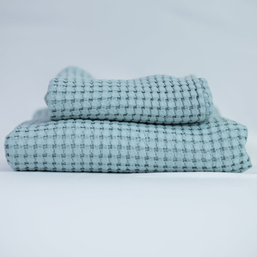 Two blue textured towels, one body and one hand, stacked against a white background