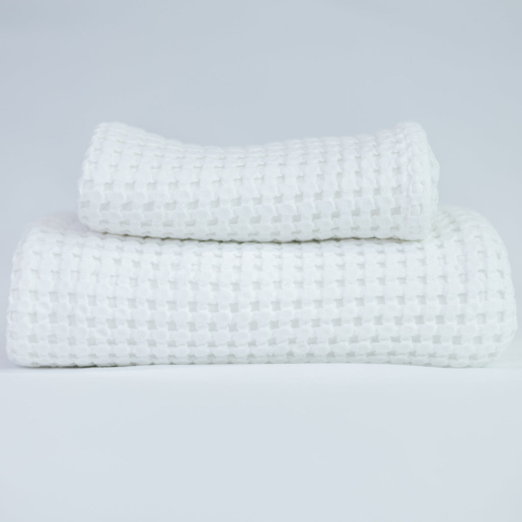 Two white textured towels, one body and one hand, stacked against a white background